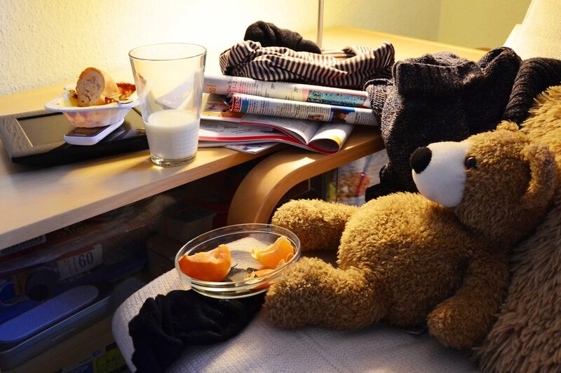 A cluttered kitchen benchtop of household clutter — stacked books, mugs, plates and soft toys waiting to be cleared