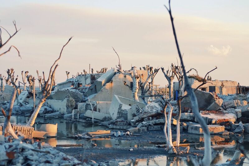 A heap of broken concrete and brick rubble with lengths of reinforcing bar and stripped vegetation mixed through it