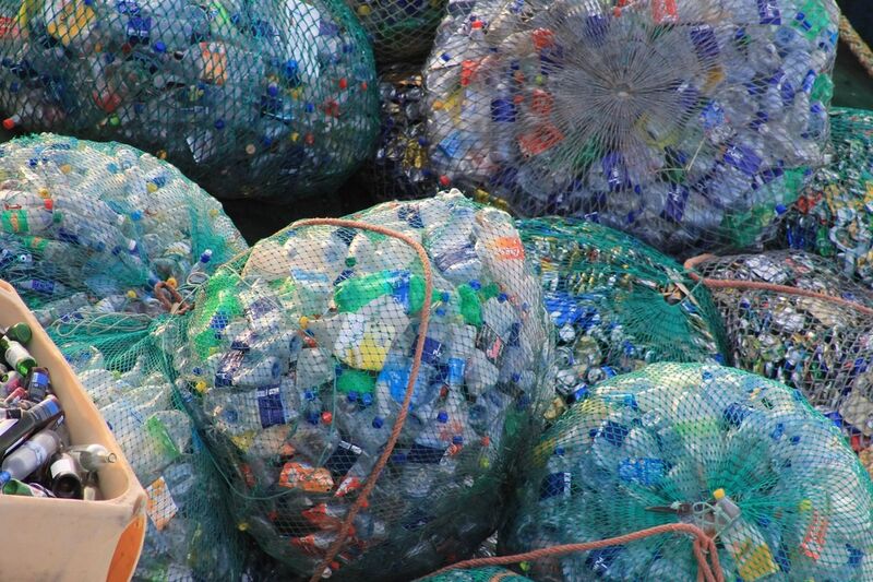 Clear plastic bags packed with crushed plastic bottles stacked at a recycling depot