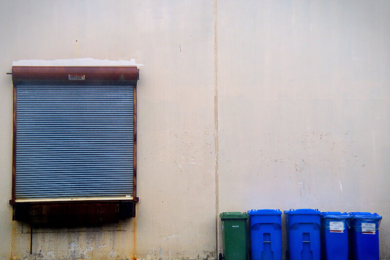 Blue, green and black wheelie bins lined up on a concrete driveway beside a roller door