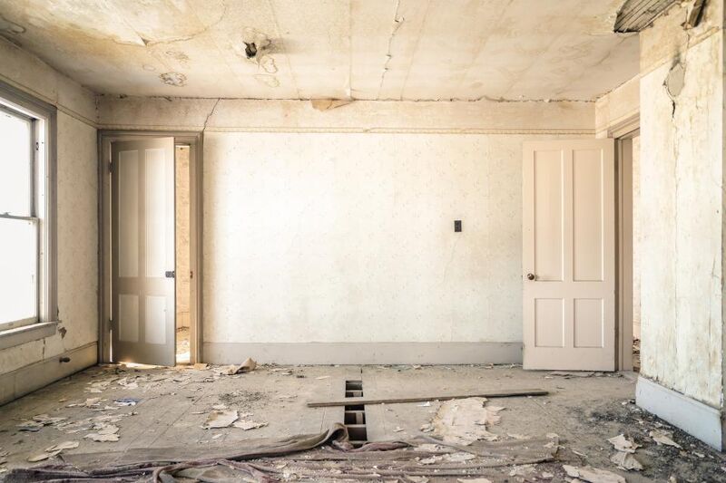 A stripped-back room mid renovation with bare walls, an open doorway and building debris on the floor